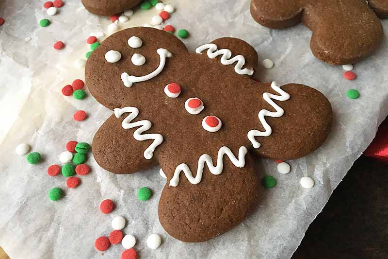 Horizontal image of a decorated gingerbread man treat on parchment paper with sprinkles.