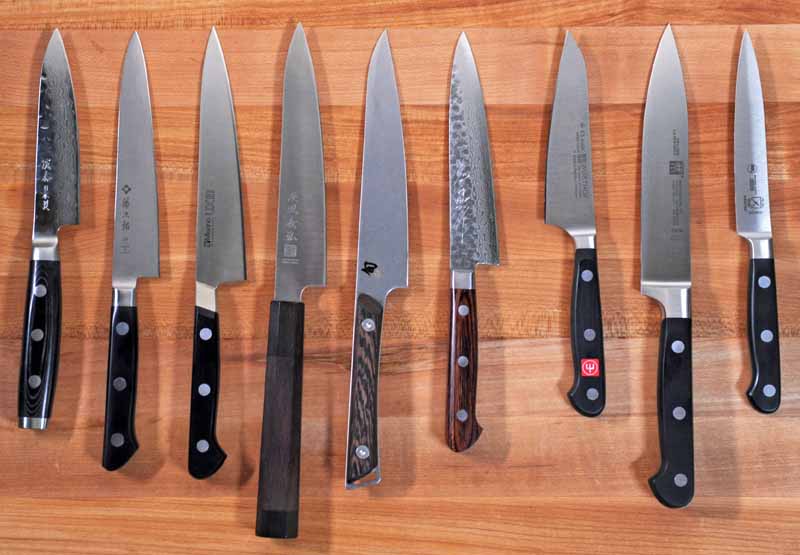 Top down view of all 9 petty and kitchen utility knives we tested. The blades are on a maple cutting board surface.