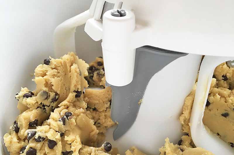 Horizontal image of part of a bowl scraper and cookie dough.