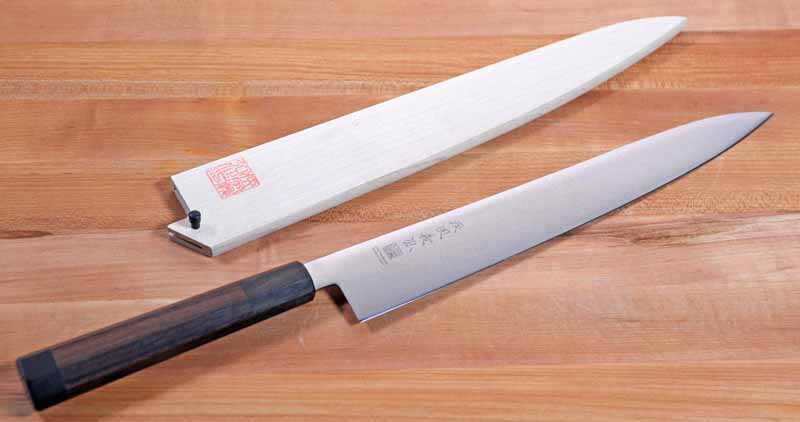 Oblique view of the Yoshihiro Ice Hardened 10.5-Inch Stainless Steel Wa Sujihiki on a medium-toned wooden butcher block surface.