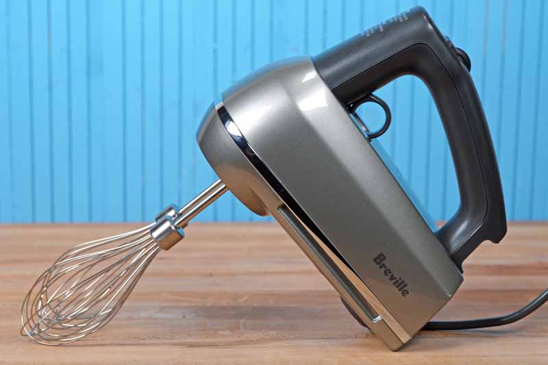 The Breville BHM800SIL Hand Mixer Review on a maple butcher block table with a blue painted wooden wall behind it.