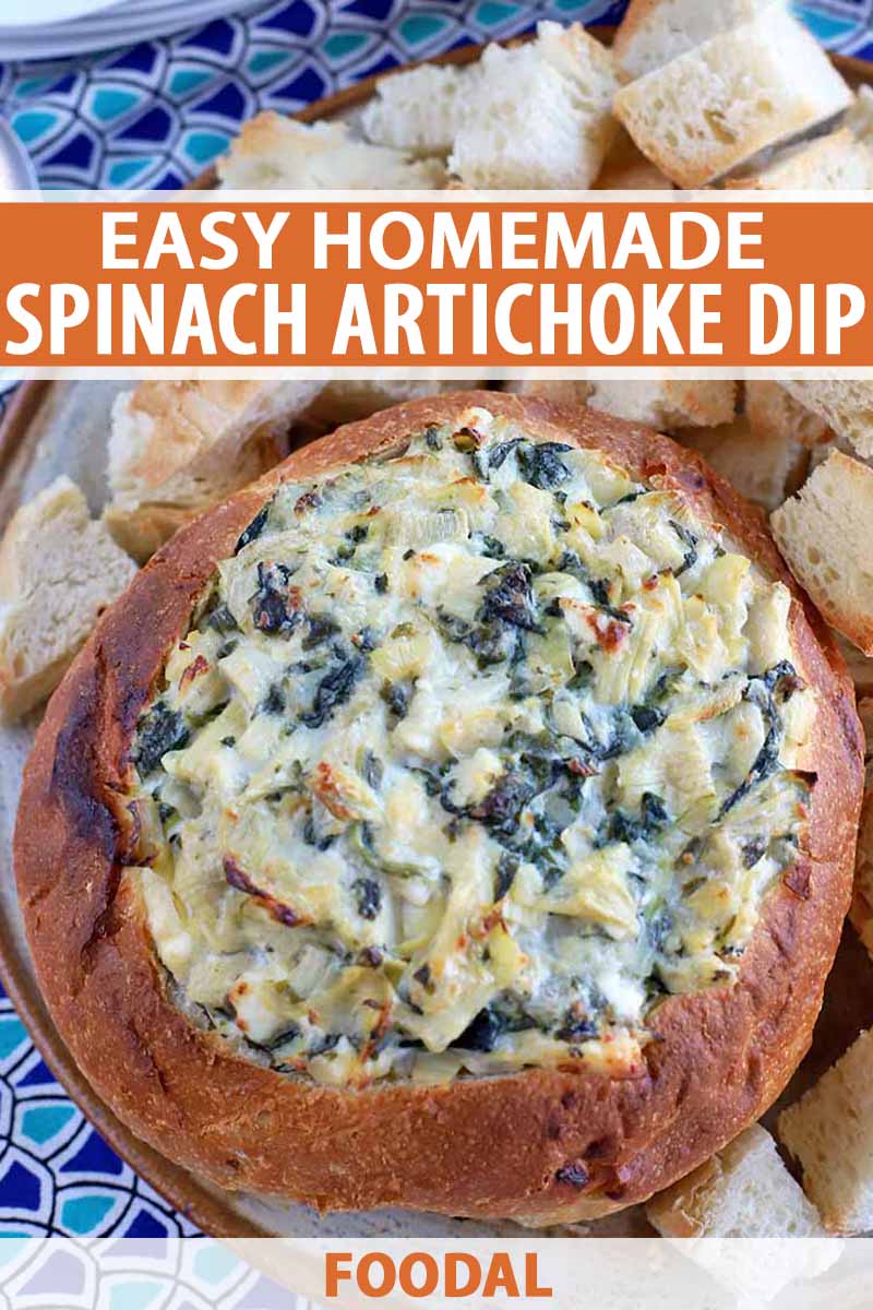 Vertical shot of a hollowed boule loaf stuffed with homemade spinach artichoke dip baked until a golden brown crust developed on top, surrounded by chunks of bread for serving on a platter, on top of a dark and light blue with a repeating triangular pattern, printed with orange and white text.