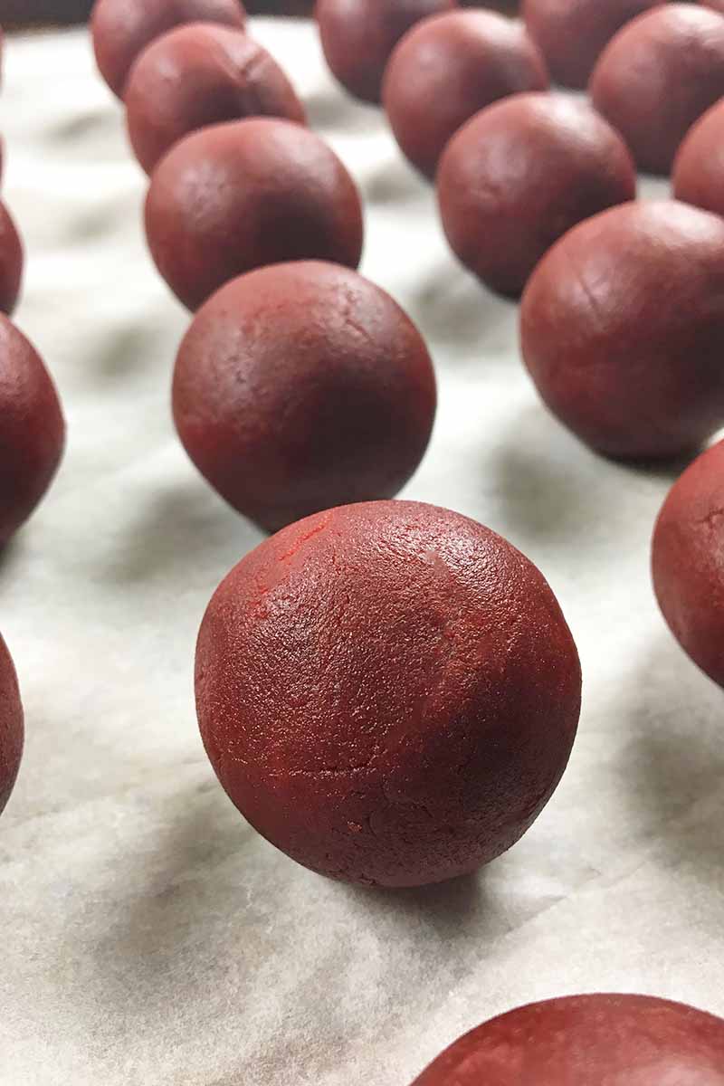 Vertical image of red velvet dessert balls on a sheet pan lined with parchment paper. 