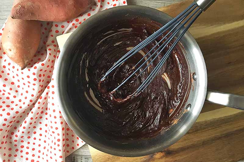 Horizontal image of a whisk mixing a thick chocolate mixture in a pot.