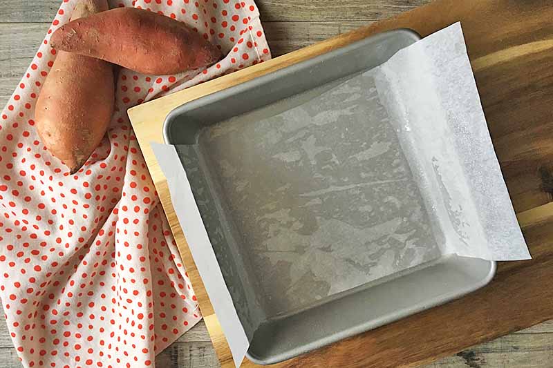 Horizontal image of a square baking dish lined with parchment paper on a wooden cutting board.