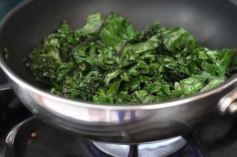 Kale sauteeing in a stainless steel pot on a gas stove.