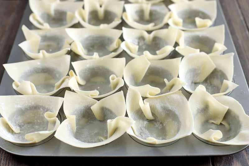 Wonton wrappers are arranged in the wells of a mini muffin tin to create cups.