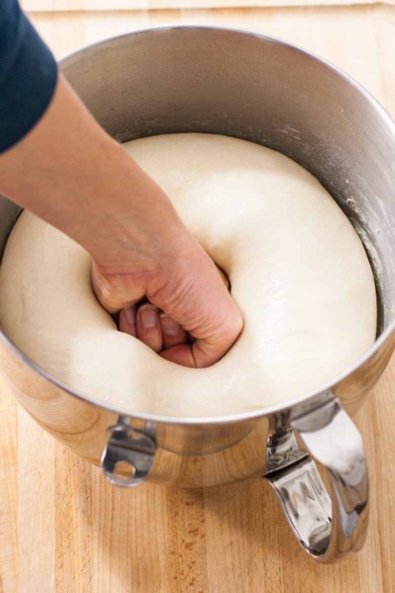 Vertical image of a hand punching down dough in a metal mixing bowl.