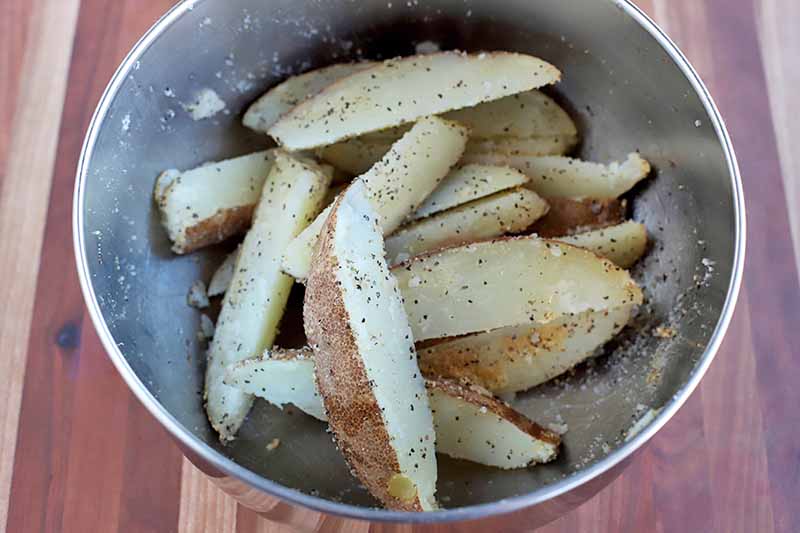 Horizontal image of uncooked sliced potatoes in a metal bowl.