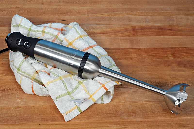 Top down of the All-Clad KZ750D Stainless Steel Immersion Blender sitting on a dish towel and maple wooden butcher board surface.