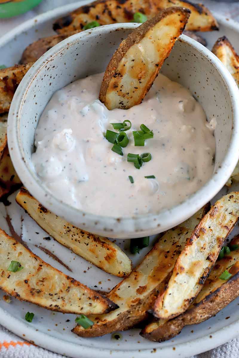 Vertical image of a bowl of creamy dip and spud wedges.