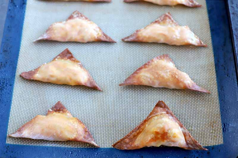 Six triangular baked wontons on a blue and white silicone baking mat.