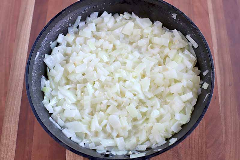 Sauteed onions nad garlic in a nonstick pan, on a striped brown wood surface.