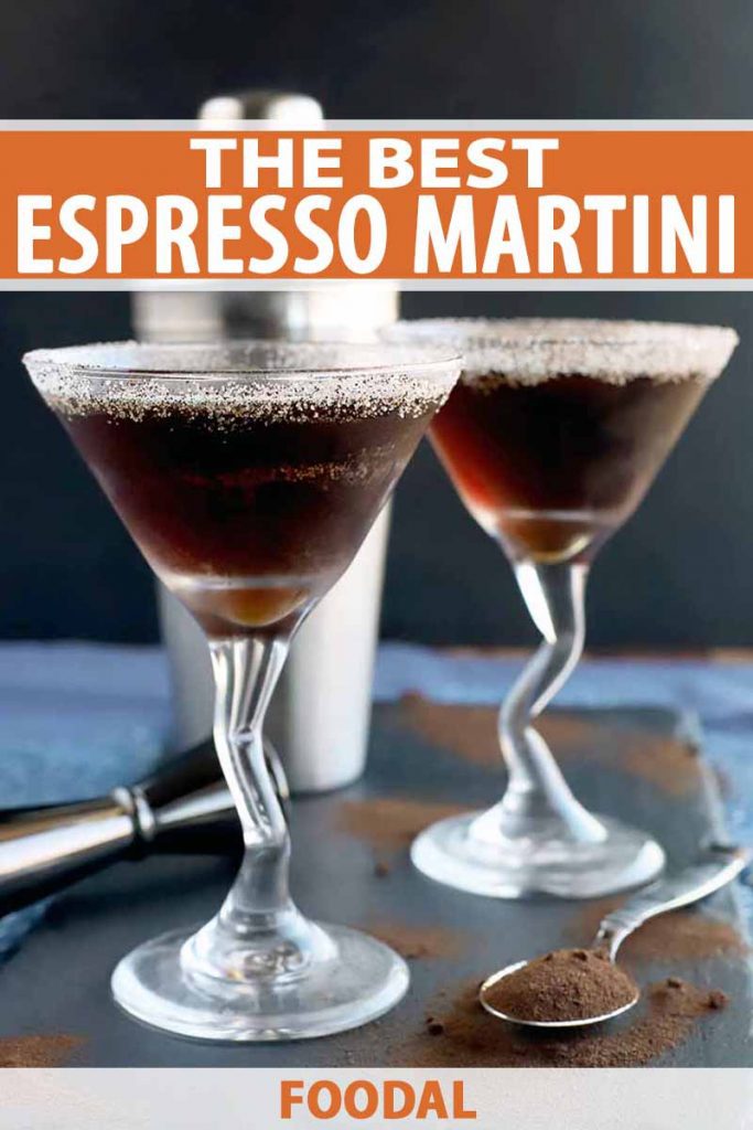 Vertical image of two espresso martinis on a slate serving platter with a stainless steel cocktail shaker and jigger, and a spoonful of coffee powder with more scattered on the surface, on a blue and white cloth with a charcoal gray background, printed with orange and white text.