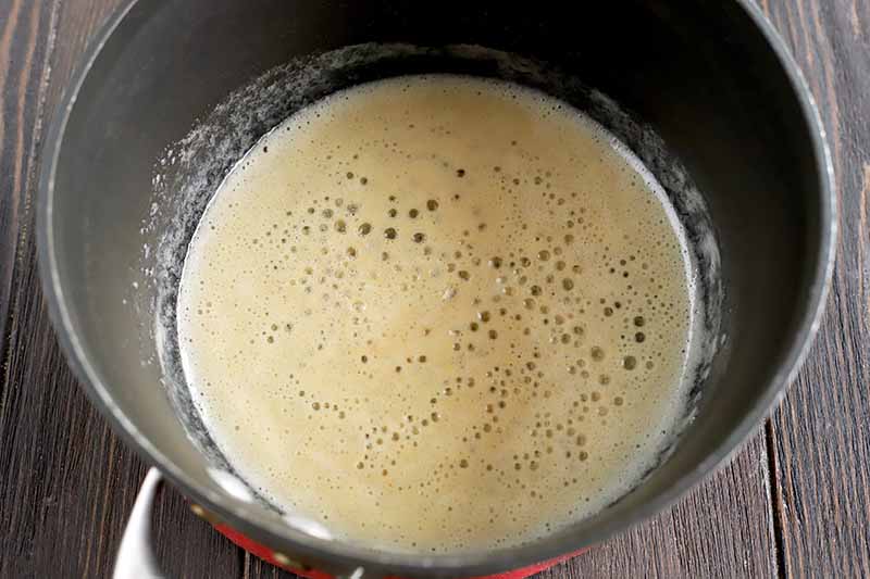 Making roux with flour and melted butter in the bottom of a nonstick saucepan, on a dark brown wood surface.