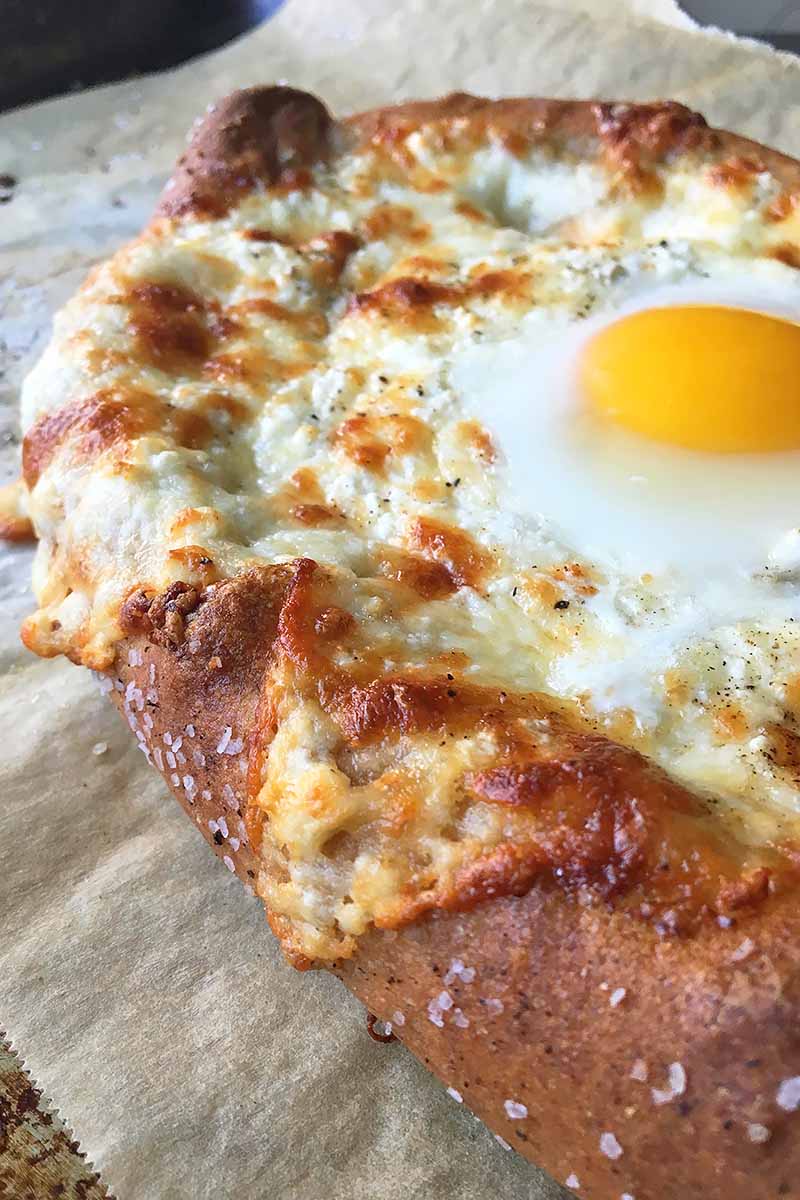 Vertical close-up image of cheese bread with an egg on top.