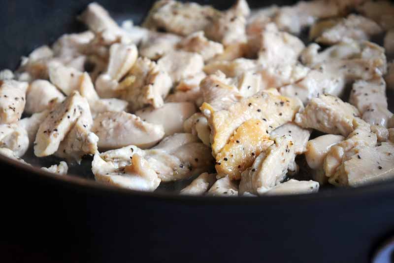 Closeup shot of cooked pieces of chicken breast in a large nonstick frying pan.