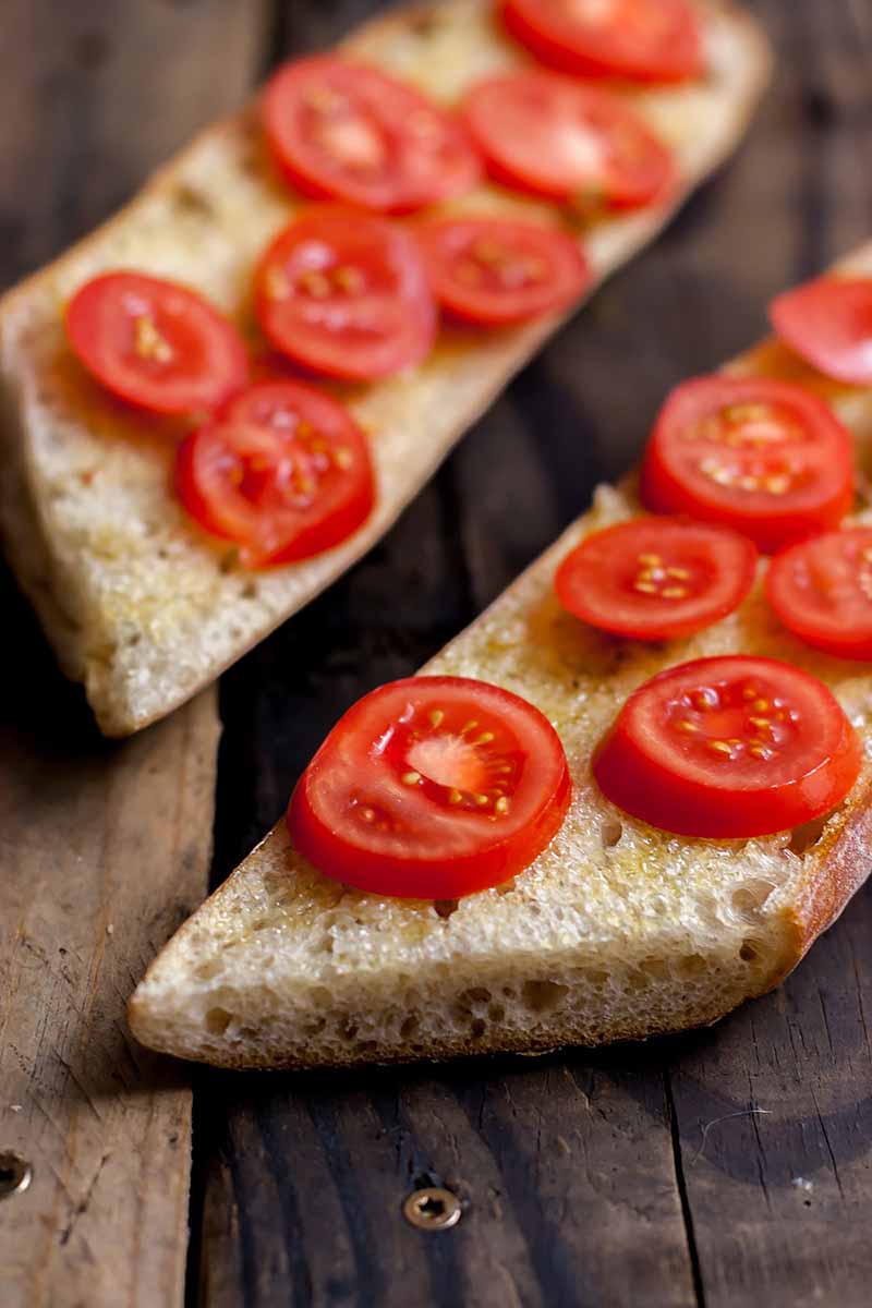 Vertical image of bread slices topped with fresh tomatoes on a wooden surface.