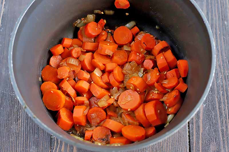 Horizontal image of cooked carrots and vegetables in a dark pot.