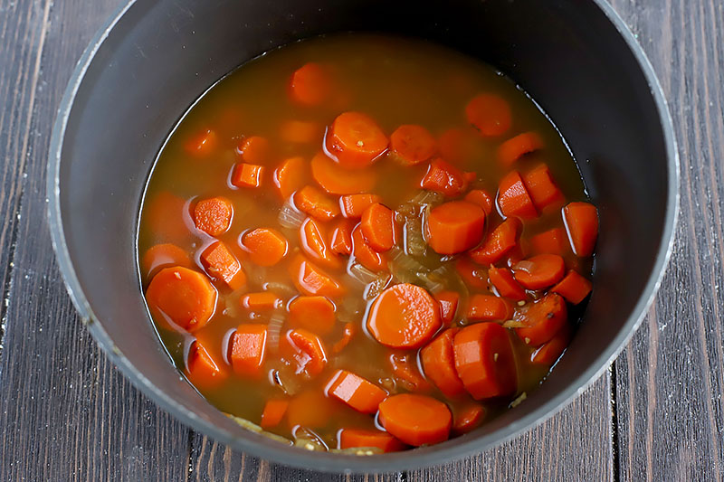 Horizontal image of sliced carrots and broth in a dark pot.