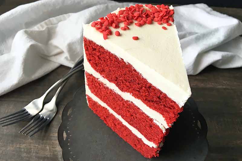 Horizontal image of a slice of red velvet cake on a gray stand.