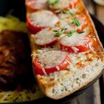 Horizontal close-up image of bread topped with cheese, tomato slices, and fresh herbs.