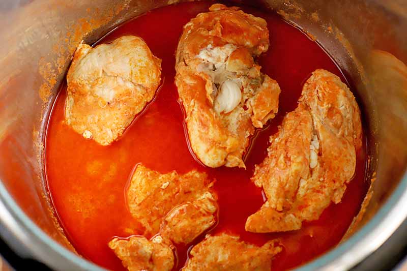 Cooked chicken and hot sauce in a metal slow cooker.