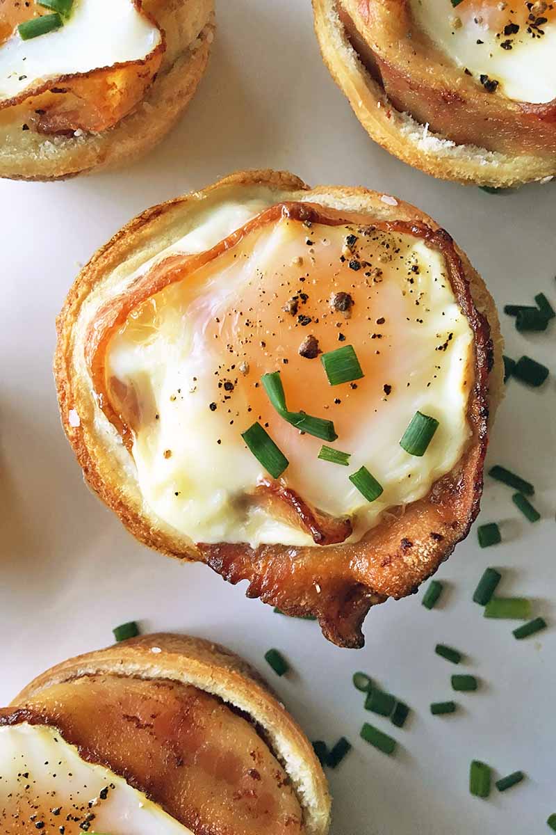 Vertical image of a breakfast dish with eggs, bacon, and white bread garnished with chives.