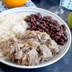 Horizontal image of a plate of pork, rice and beans next to whole citrus.