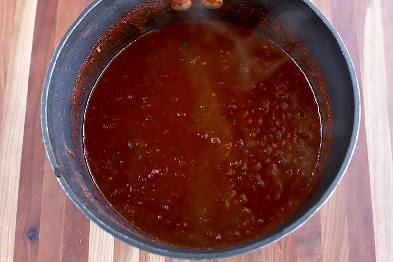 Horizontal image of a hot red sauce in a pot.