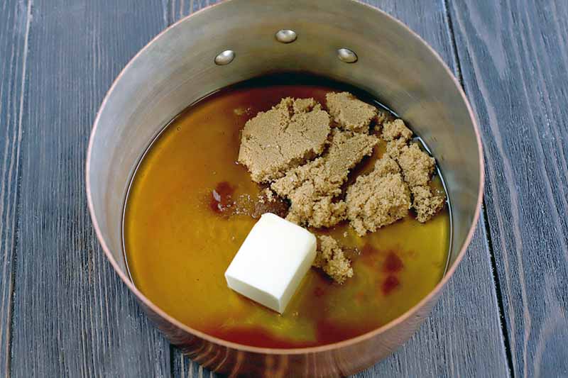 Melted and solid butter and brown sugar in a stainless steel bowl with a ring handle, on a dark brown wood surface.