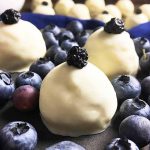 Horizontal image of candies with white chocolate coatings and dried and fresh blueberries.