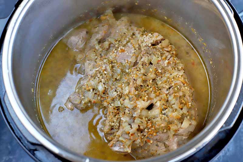 Horizontal image of cooked pork and its juices in a slow cooker.