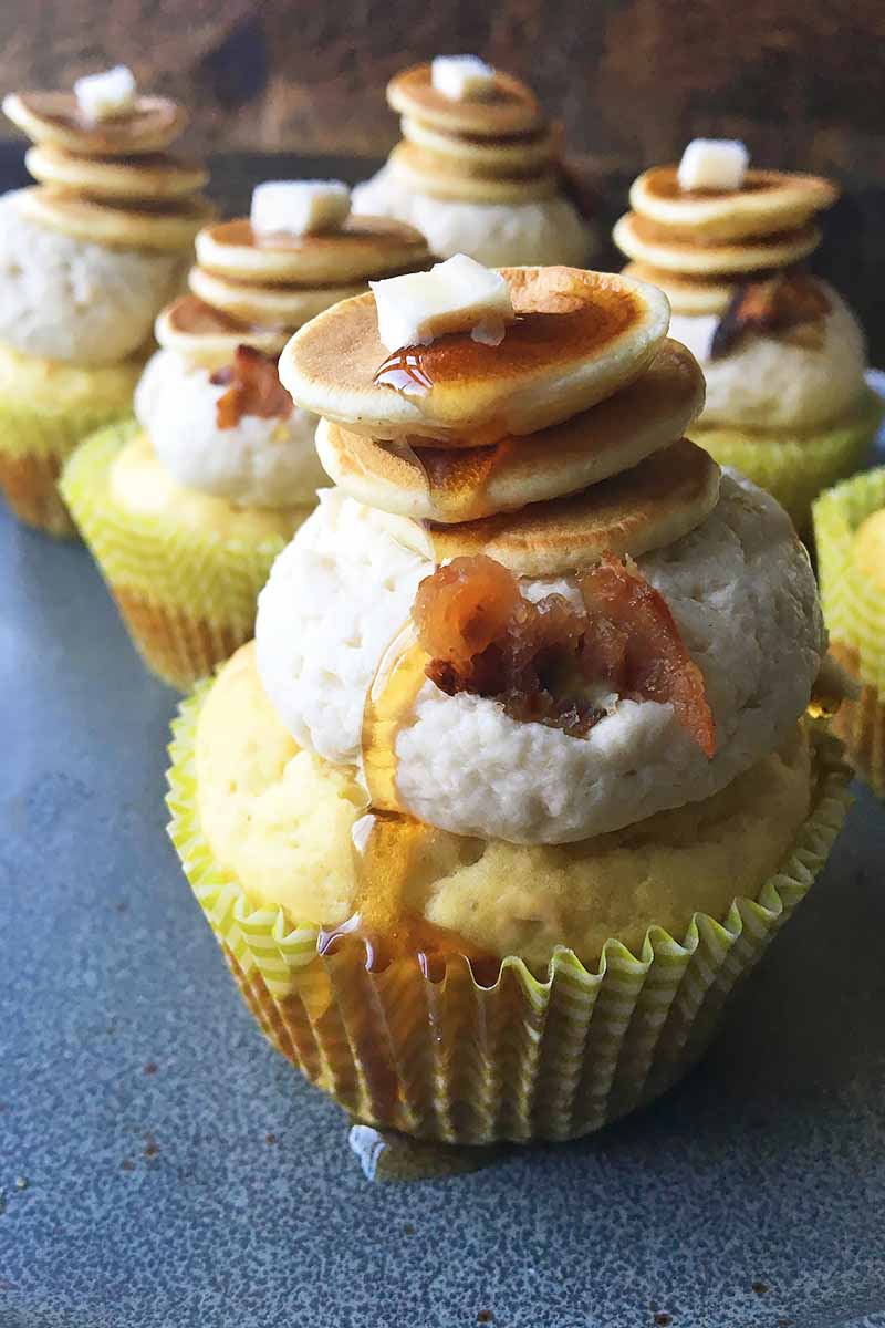 Vertical image of cupcakes with pancakes and butter on top with maple syrup dribbling on the side.