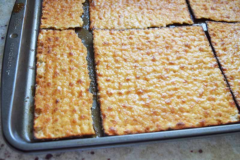 Matzo arranged on a baking sheet to fill a metal baking pan, with homemade toffee baked into the top.