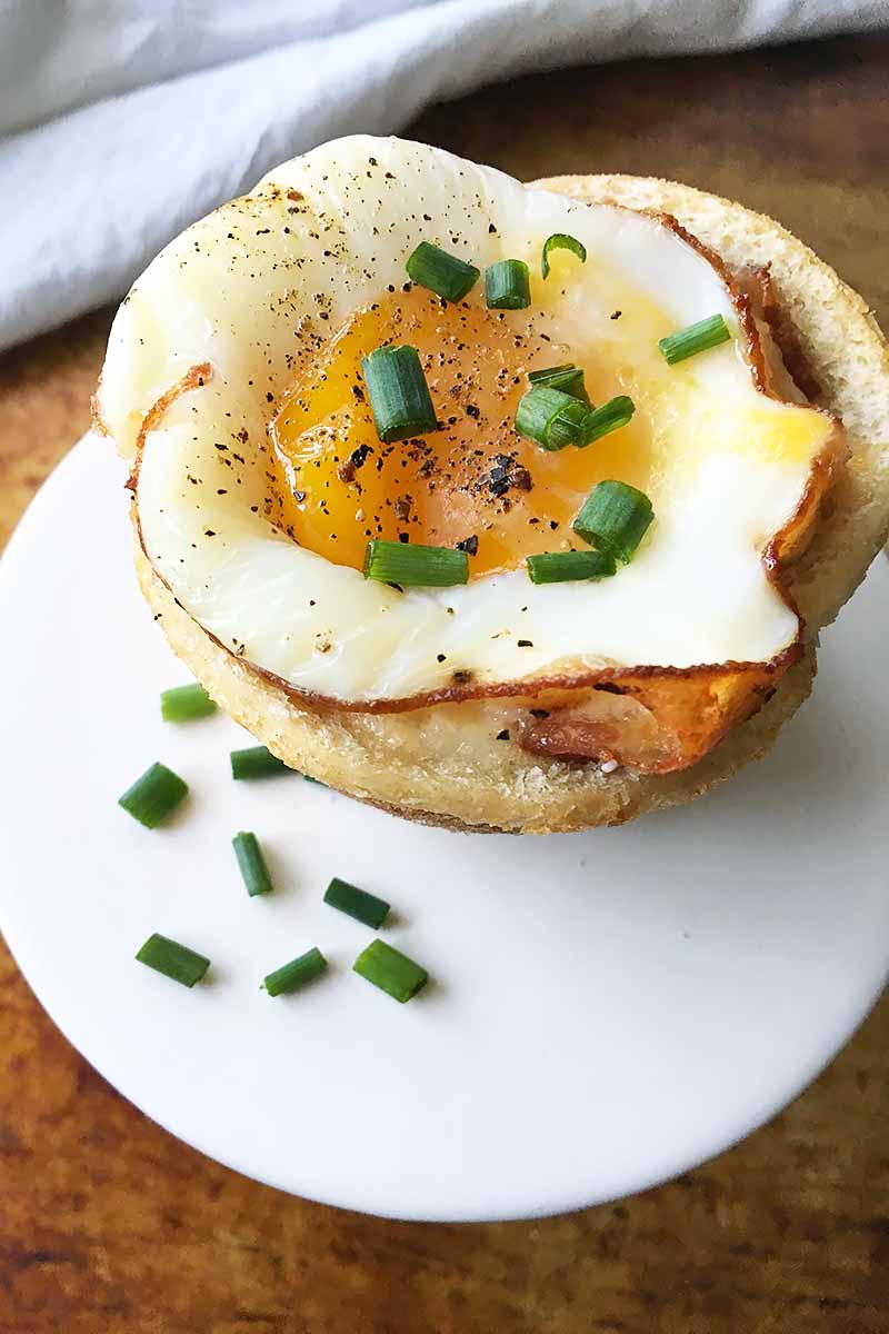 Vertical image of one breakfast dish with a whole baked egg and chive garnish.