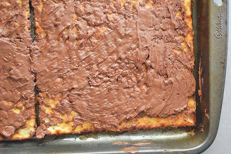 Closeup closely cropped horizontal image of melted chocolate spread on top of matzo with toffee on a metal rimmed baking sheet.
