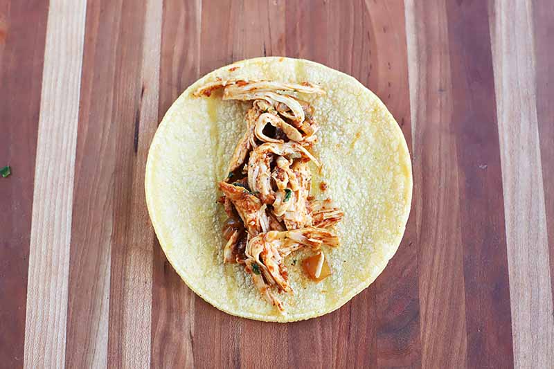Horizontal image of a tortilla shell and shredded chicken in the middle.