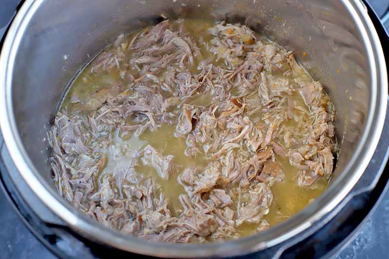 Horizontal image of shredded pork and its juices in a slow cooker.