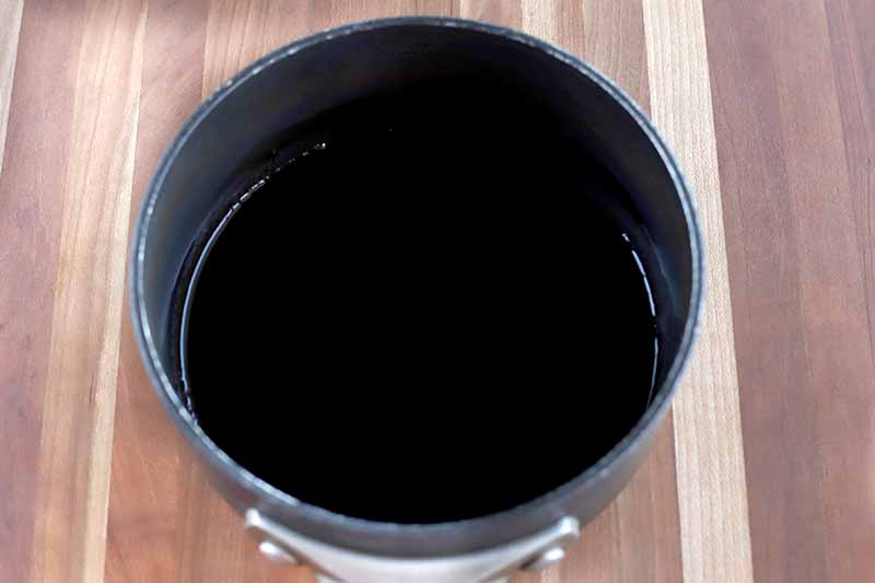 Closely cropped overhead horizontal shot of balsamic vinegar in a nonstick saucepan, on a dark and light brown striped wood surface.