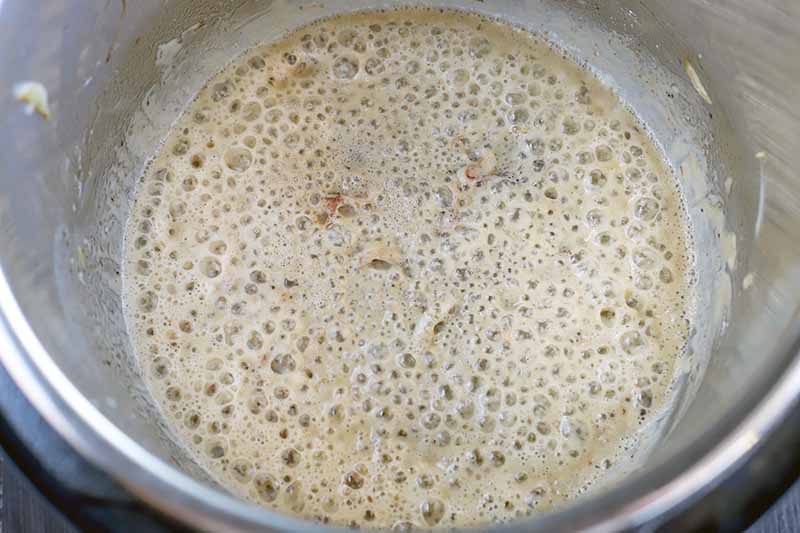 Overhead shot of frothy melted butter in the bottom of a metal Instant Pot insert, on a dark brown wood background.