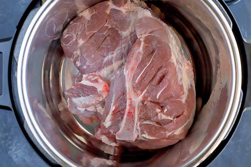Horizontal image of raw pork in a slow cooker.