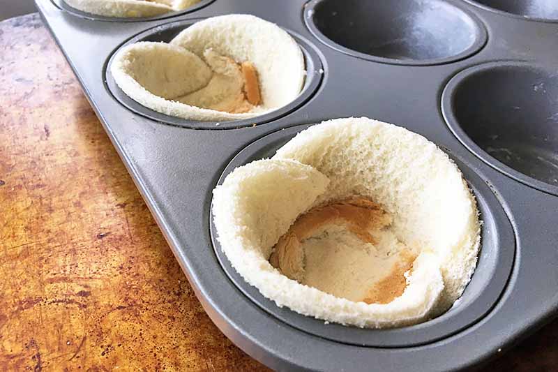 Horizontal image of a muffin tin with some cups lined with rolled out white bread.
