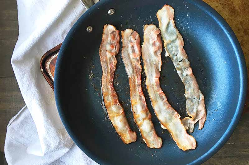 Horizontal image of bacon cooking in a skillet.