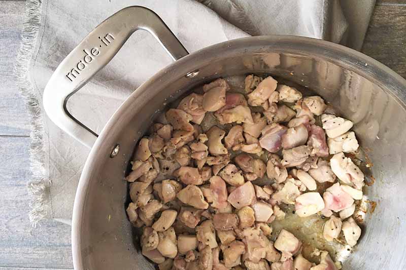 Horizontal image of cooking chopped chicken in a pot.