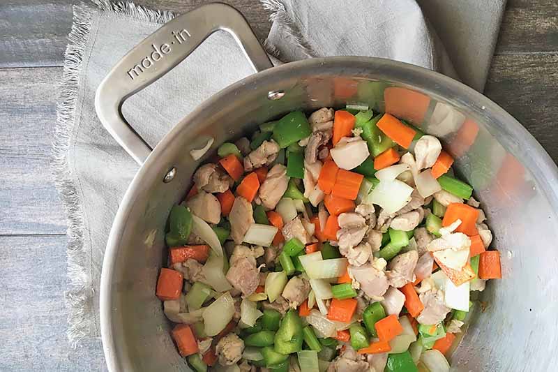 Horizontal image of assorted vegetables and chopped chicken in a pot.