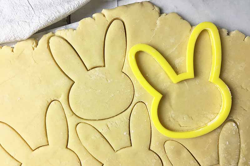 Horizontal image of a yellow rabbit-shaped cut-out tool on flattened dough with cut-outs.