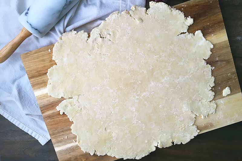 Horizontal image of a rolled out pie dough on a wooden cutting board.