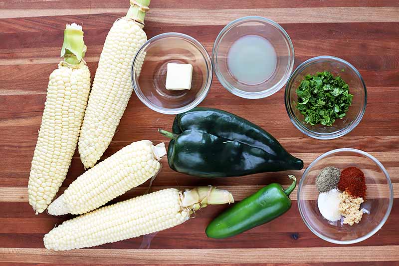 Horizontal image of assorted ingredients including peppers and corn on a wooden cutting board.
