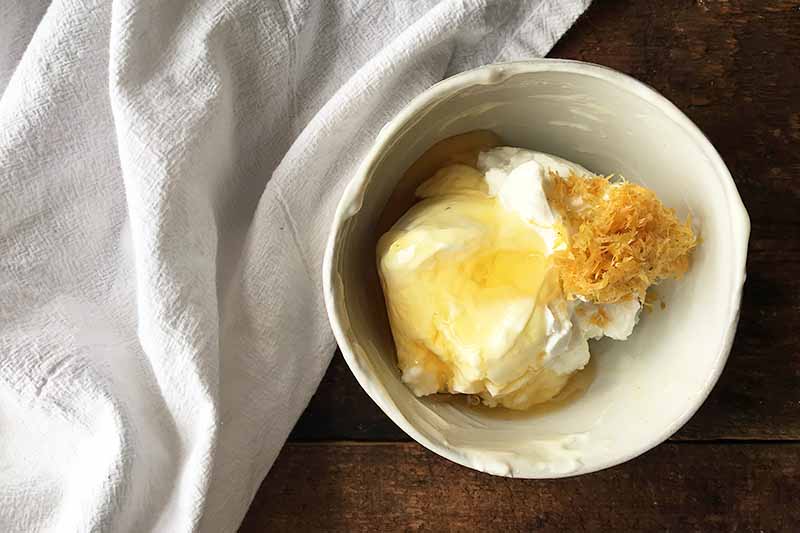Horizontal image of a bowl with yogurt, honey, and citrus zest next to a white towel.